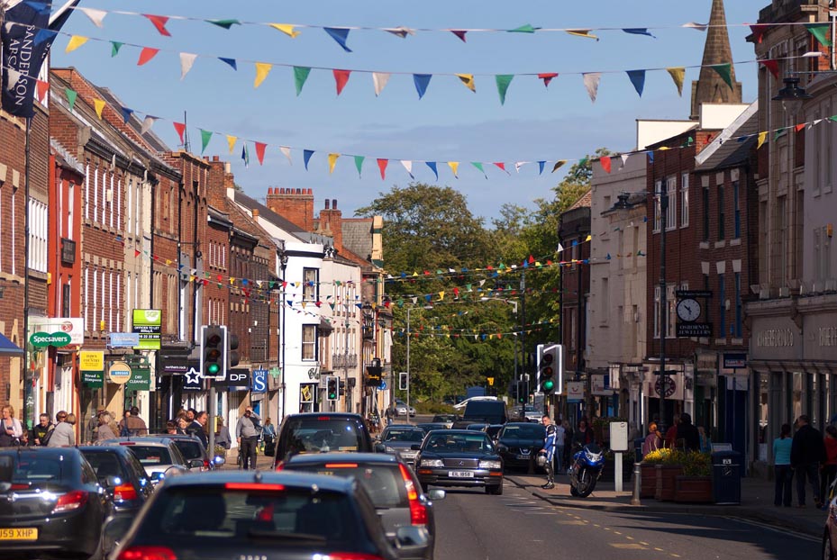 Image shows Morpeth's High Street on a sunny day with bunting flying overhead across the road.