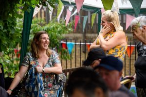 Two people sit outside with bunting, smiling together. (c) Alex Brennan